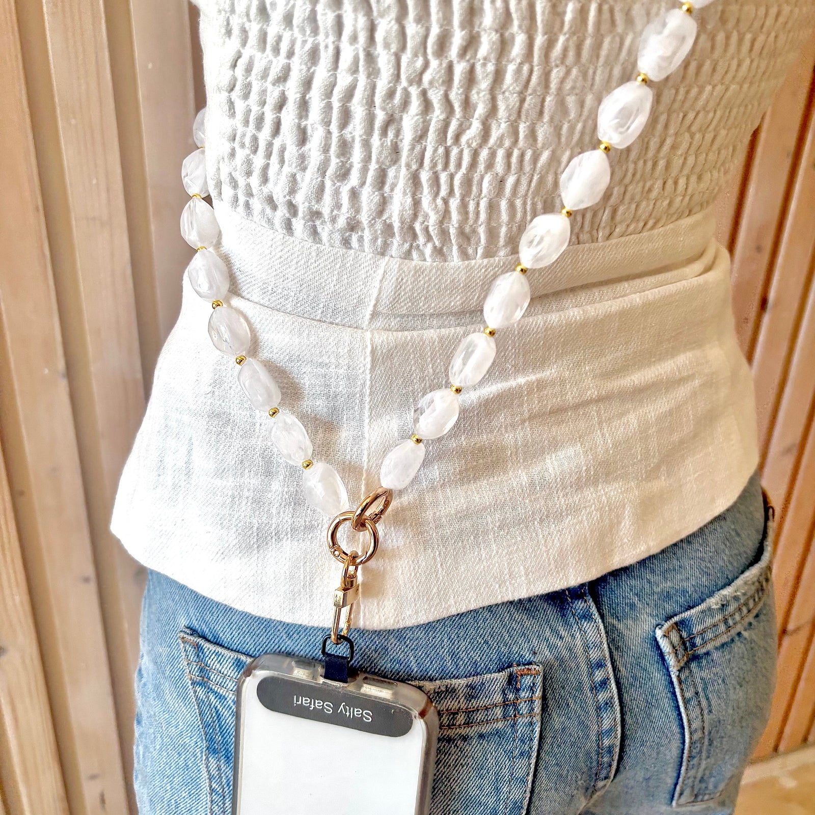 Person wearing a beaded necklace with a phone holder attached, standing indoors.